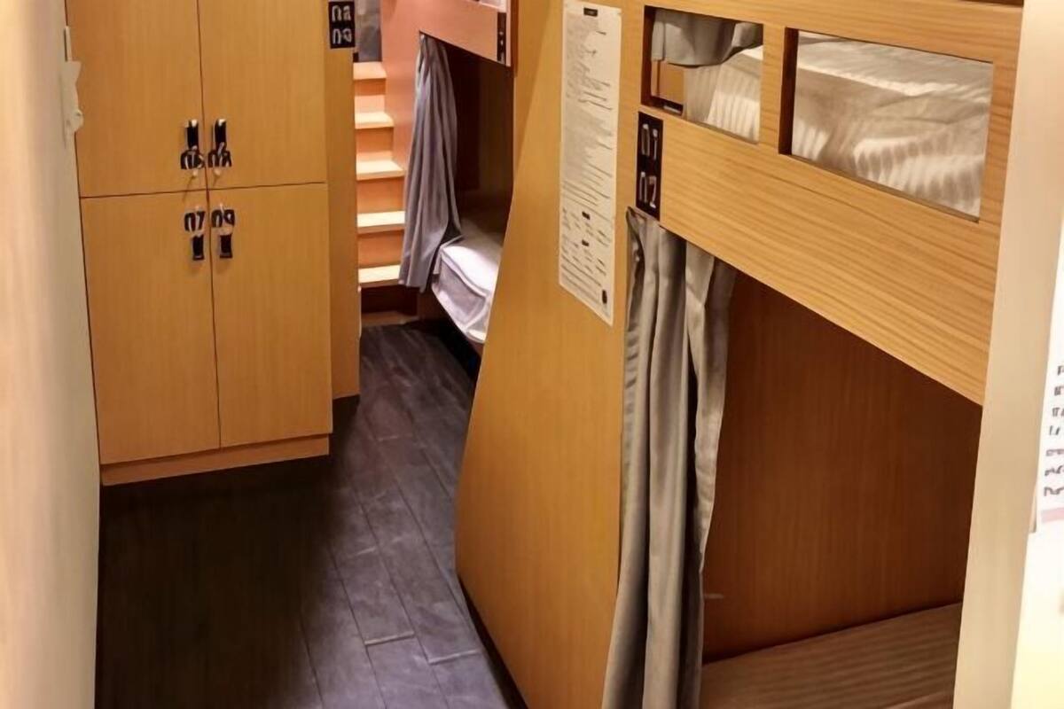 A narrow room with a bunk bed, wooden wardrobe, and a small window.