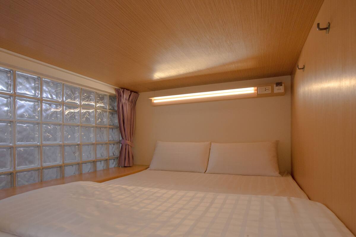 A bedroom with a large window, a bed with white bedding, and a wooden ceiling.