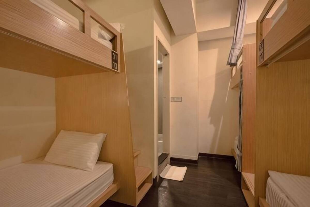 A narrow hotel corridor with bunk beds on either side, a door at the end, and a small rug on the floor.