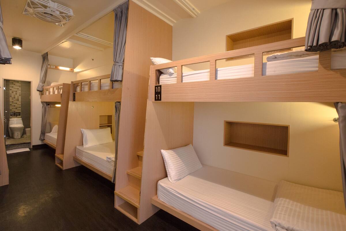 A dormitory-style room with bunk beds, a small shelf, and a shower area.