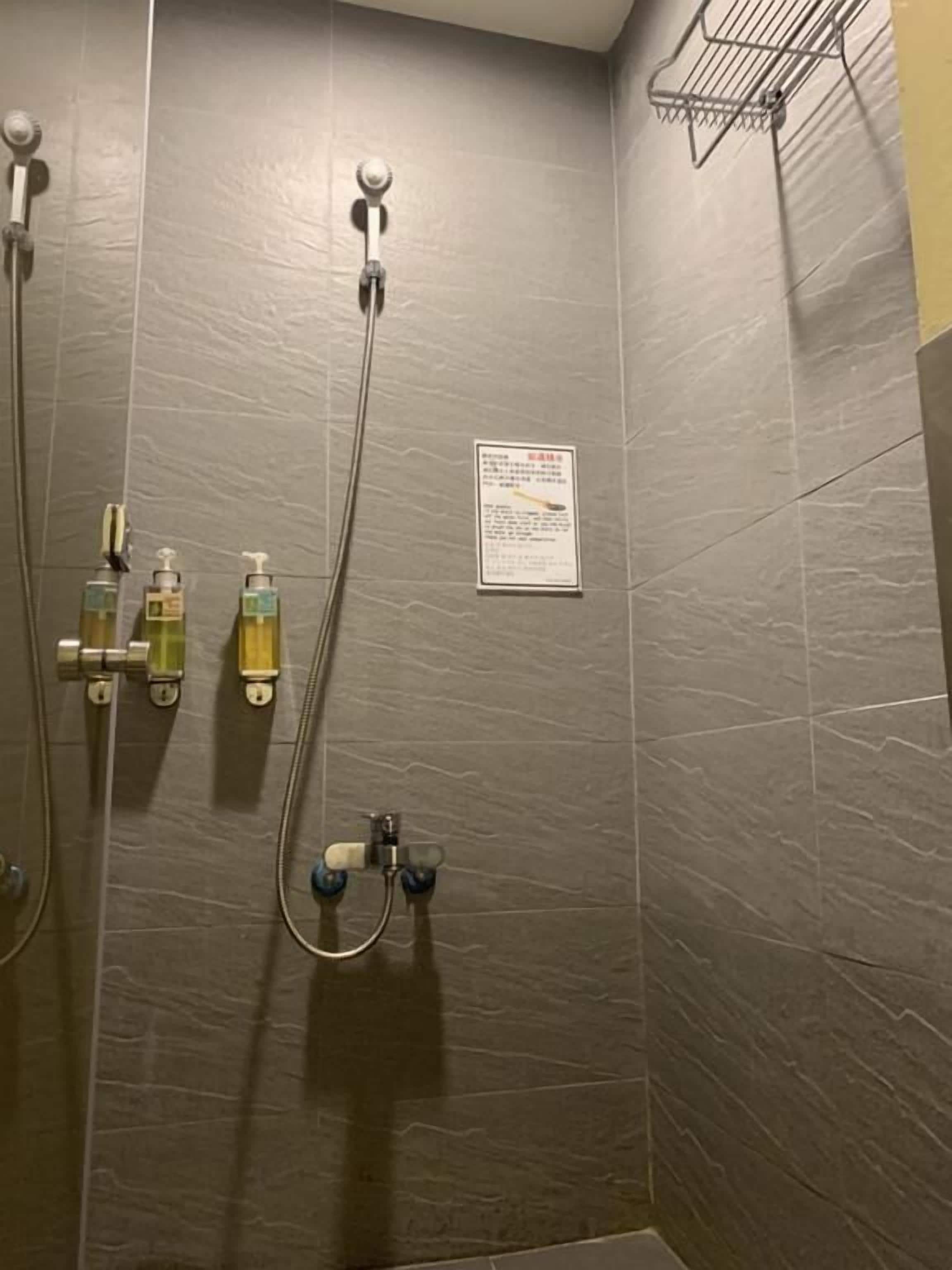 A shower area with grey tiles, a hand shower, a wall-mounted hand dryer, and a soap dispenser.