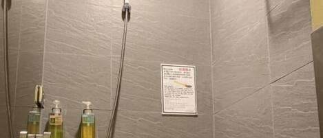 A shower area with grey tiles, a hand shower, a wall-mounted hand dryer, and a soap dispenser.