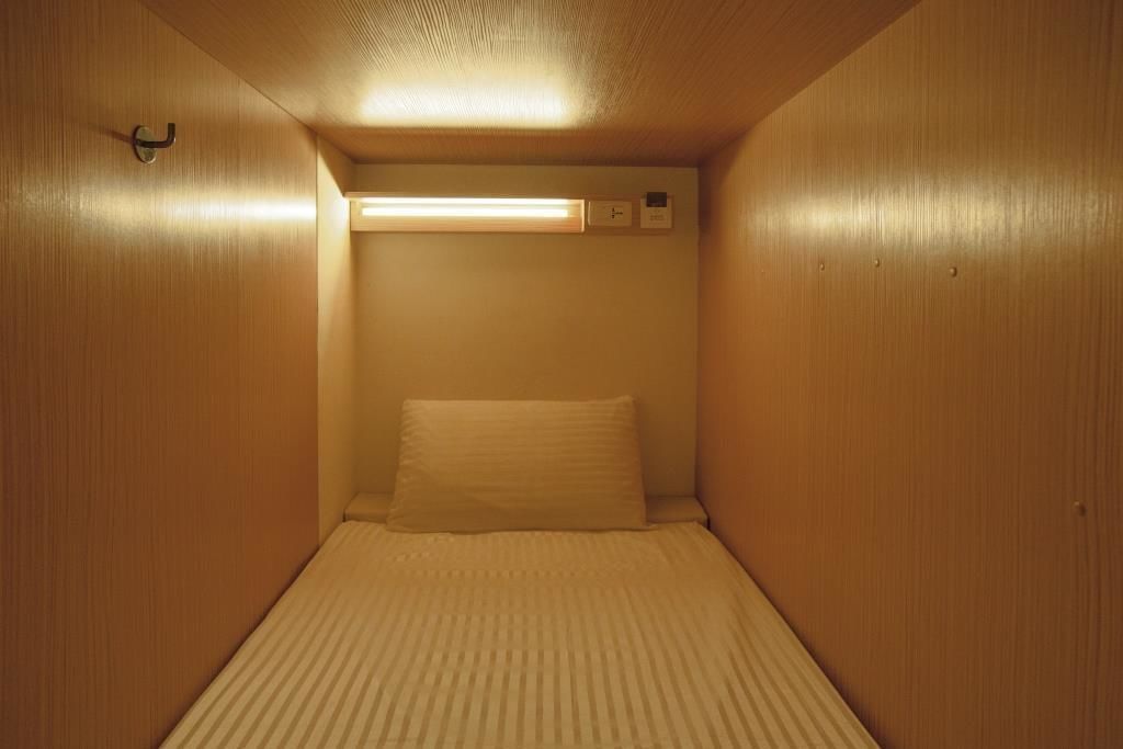 Una habitación pequeña y privada con una cama individual, una lámpara fijada a la pared y un termostato.