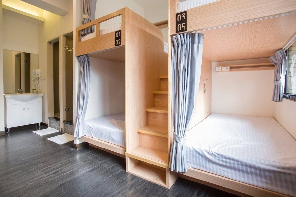 A hotel room with bunk beds, a bathroom with a sink and mirror, and a small desk.