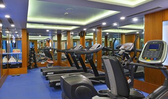 Uma academia com várias esteiras, aparelhos de musculação e um espelho grande na parede.