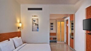Habitación de hotel con una cama grande, un televisor montado en la pared, un cuadro y un pasillo que conduce a un baño.