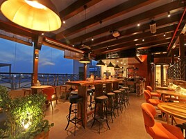 Restaurante com área de bar, tetos altos e grandes janelas com vista para a paisagem urbana.