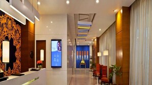 Un moderno vestíbulo de hotel con un mostrador de recepción, una pantalla digital, una pared azul con paneles verticales y zonas de estar.