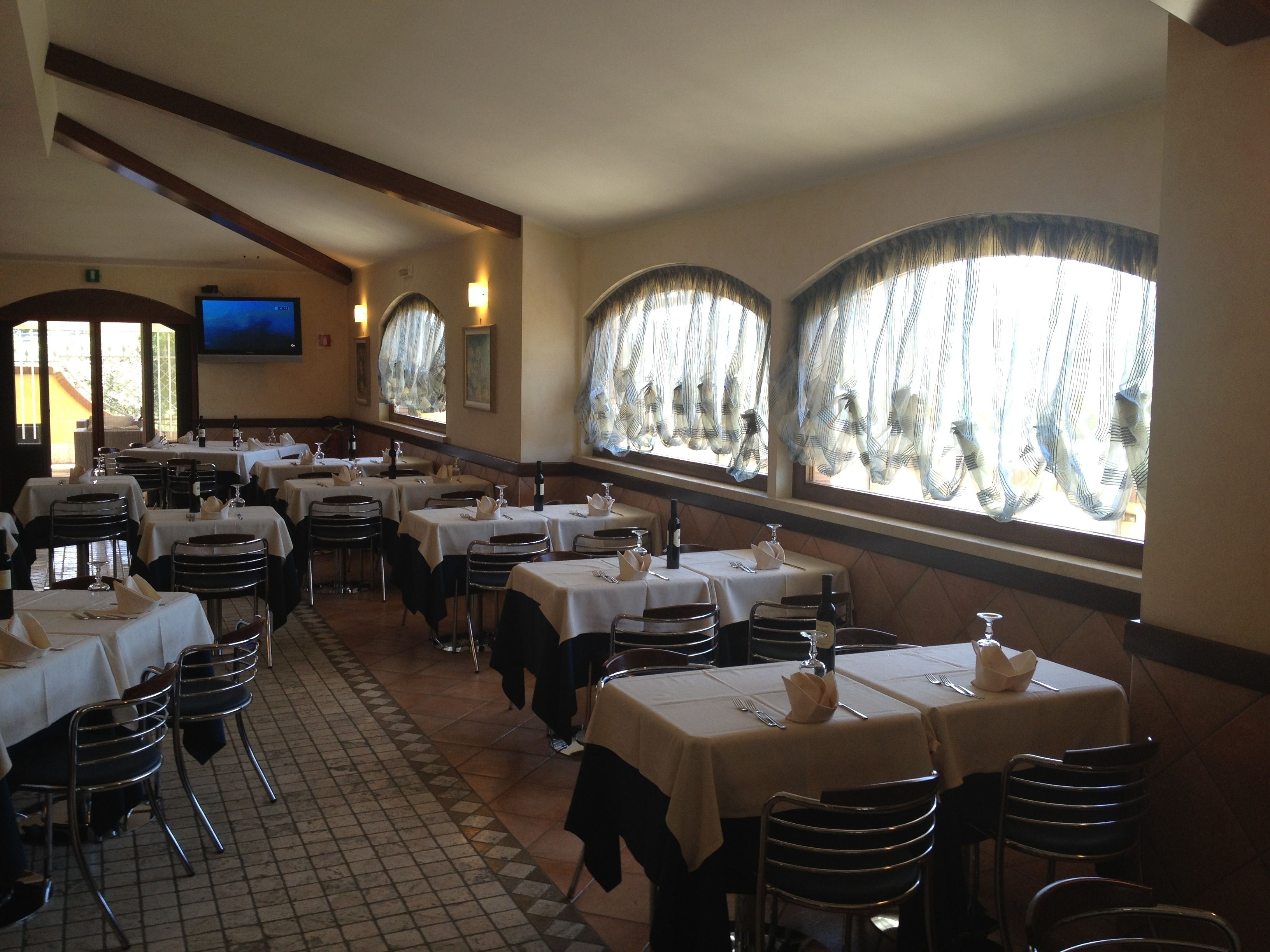 A restaurant with multiple tables, chairs, and large windows with curtains.