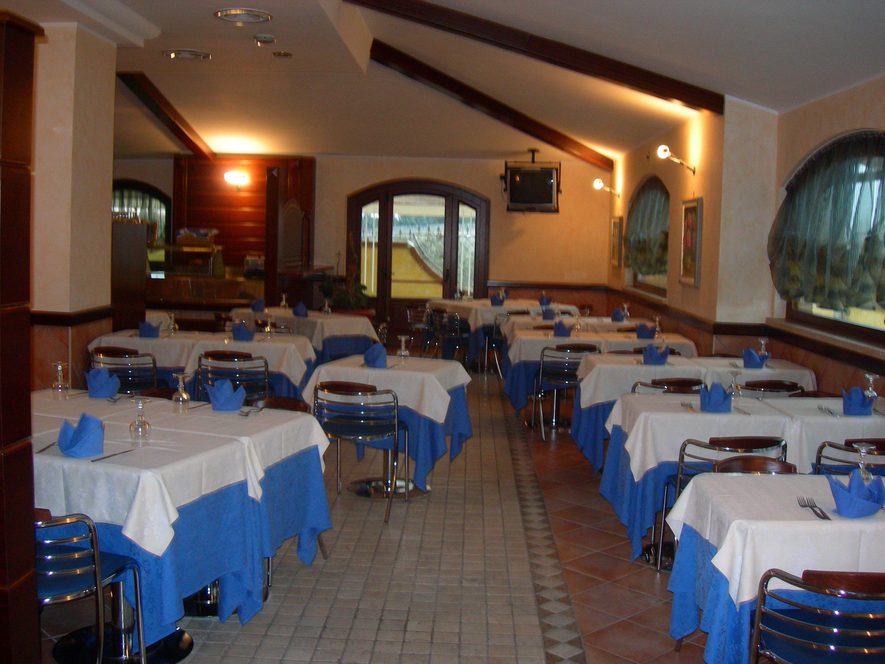 A restaurant with multiple tables, each covered with a white tablecloth and blue napkins.