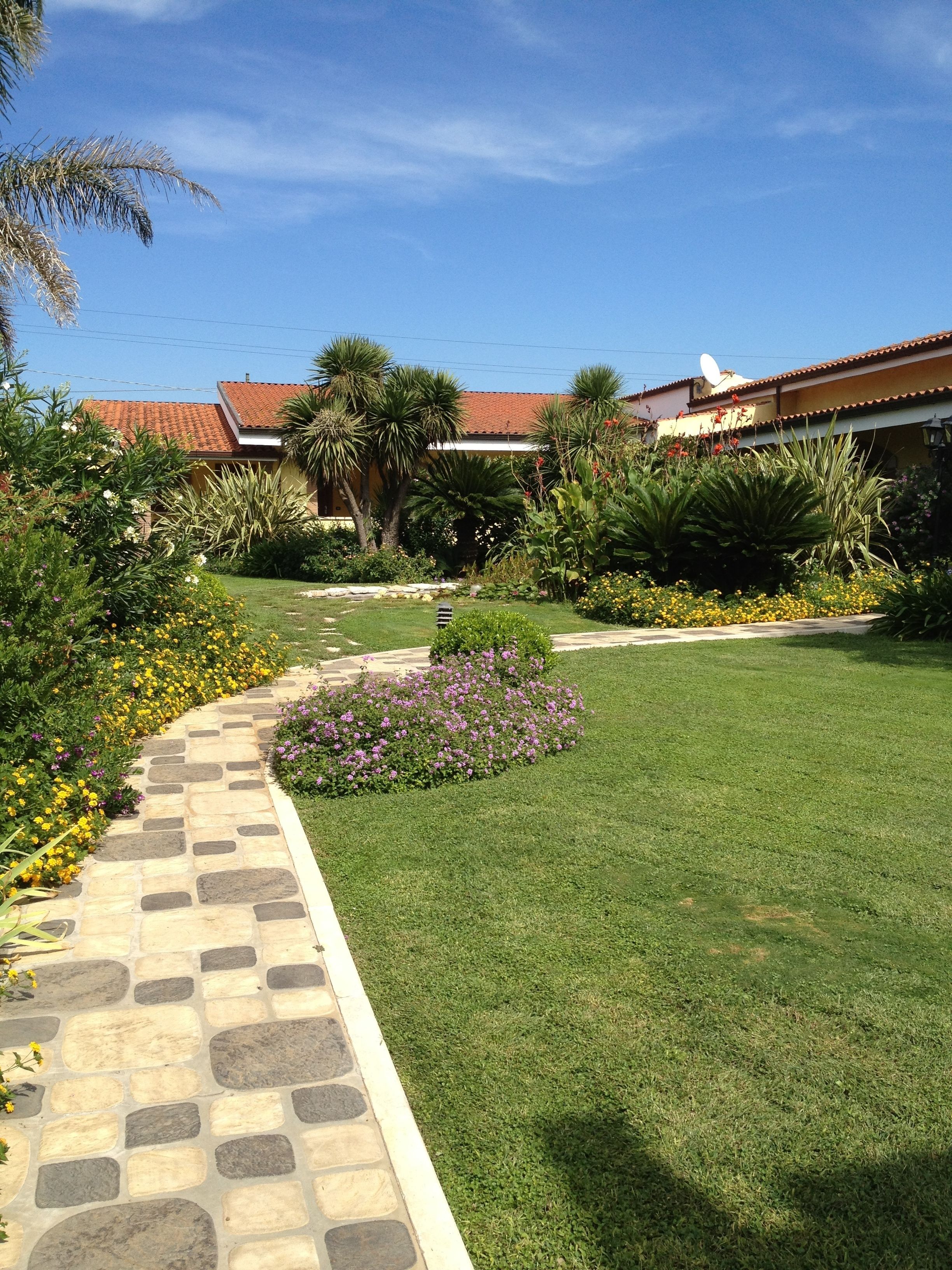 A well-maintained garden with a stone pathway leading to a building with a red-tiled roof.