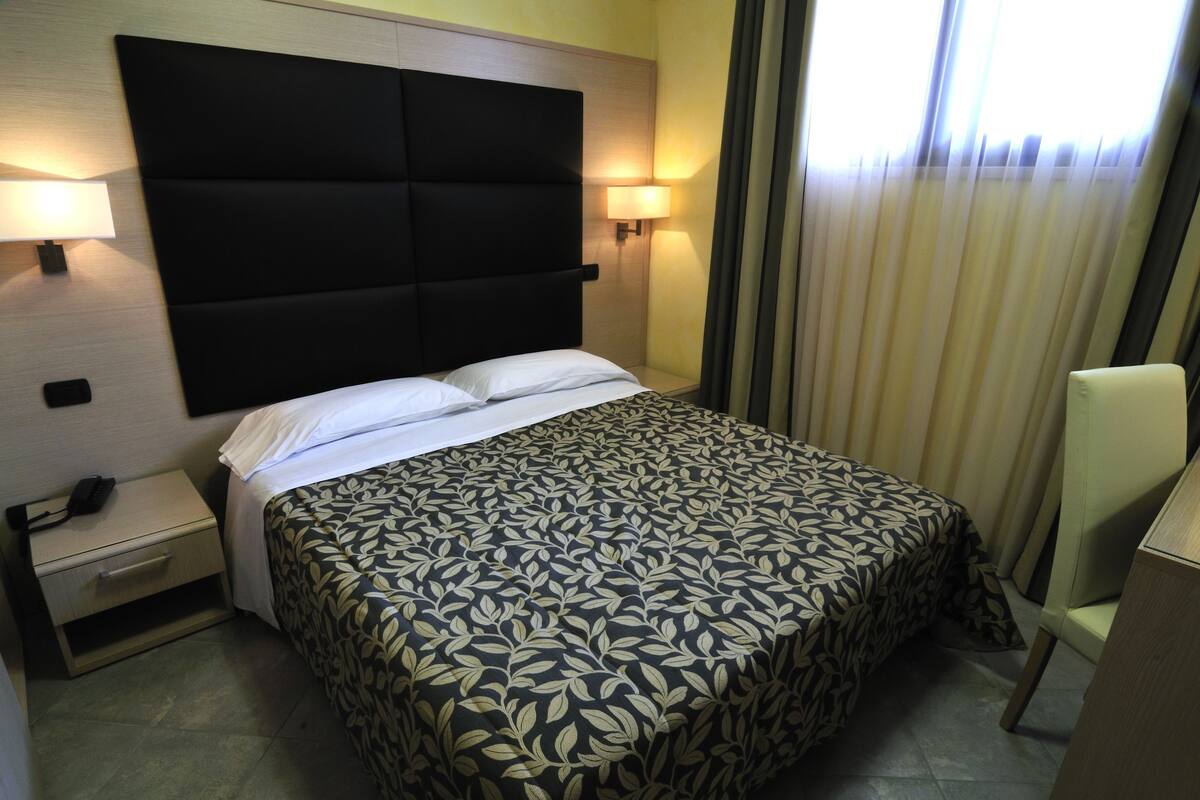 Une chambre d’hôtel avec un grand lit, des lampes de chevet, une table de chevet avec un téléphone et une chaise.