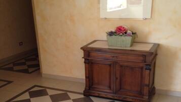 A checkered floor, a wooden cabinet with a flower basket, and a bulletin board on a beige wall.