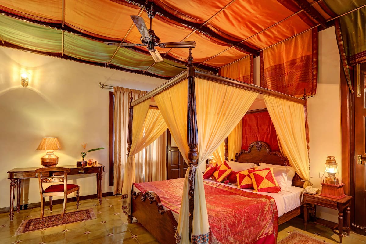 Ein Bett mit Himmelbett, ein Holztisch mit Lampe und ein Nachttisch ebenfalls mit Lampe.