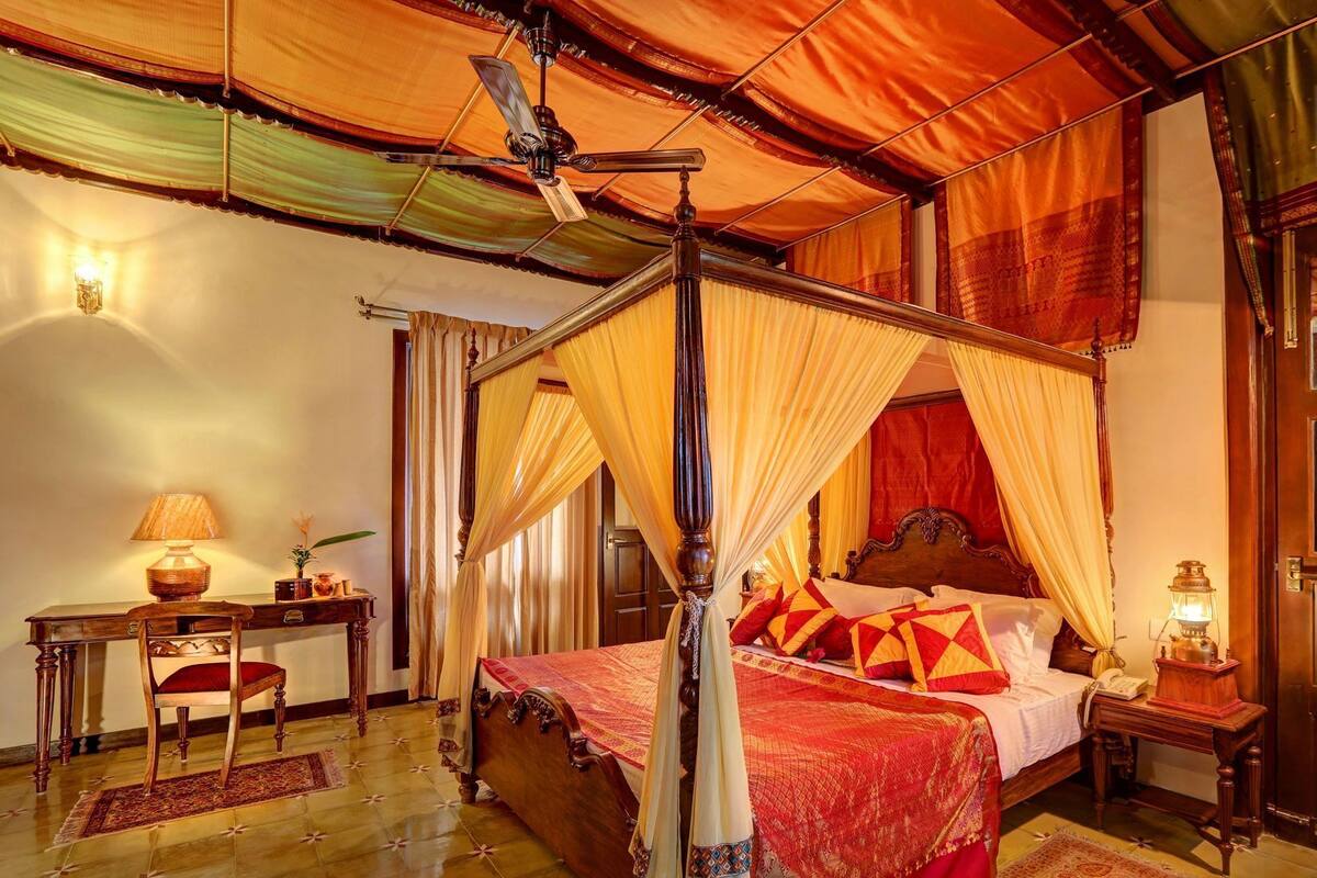 Ein Bett mit Baldachin, ein Holztisch mit Lampe und ein Nachttisch ebenfalls mit Lampe.
