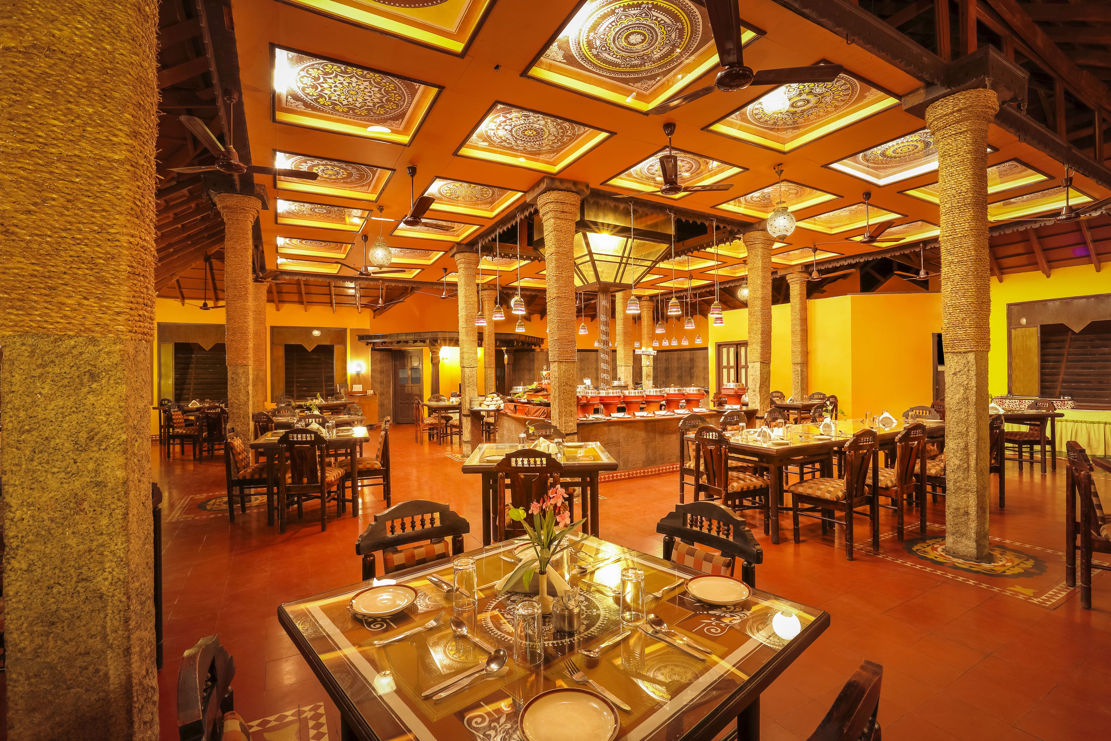 A restaurant with high ceilings, ornate ceiling designs, and a central bar area. Tables are set with fine dining ware.