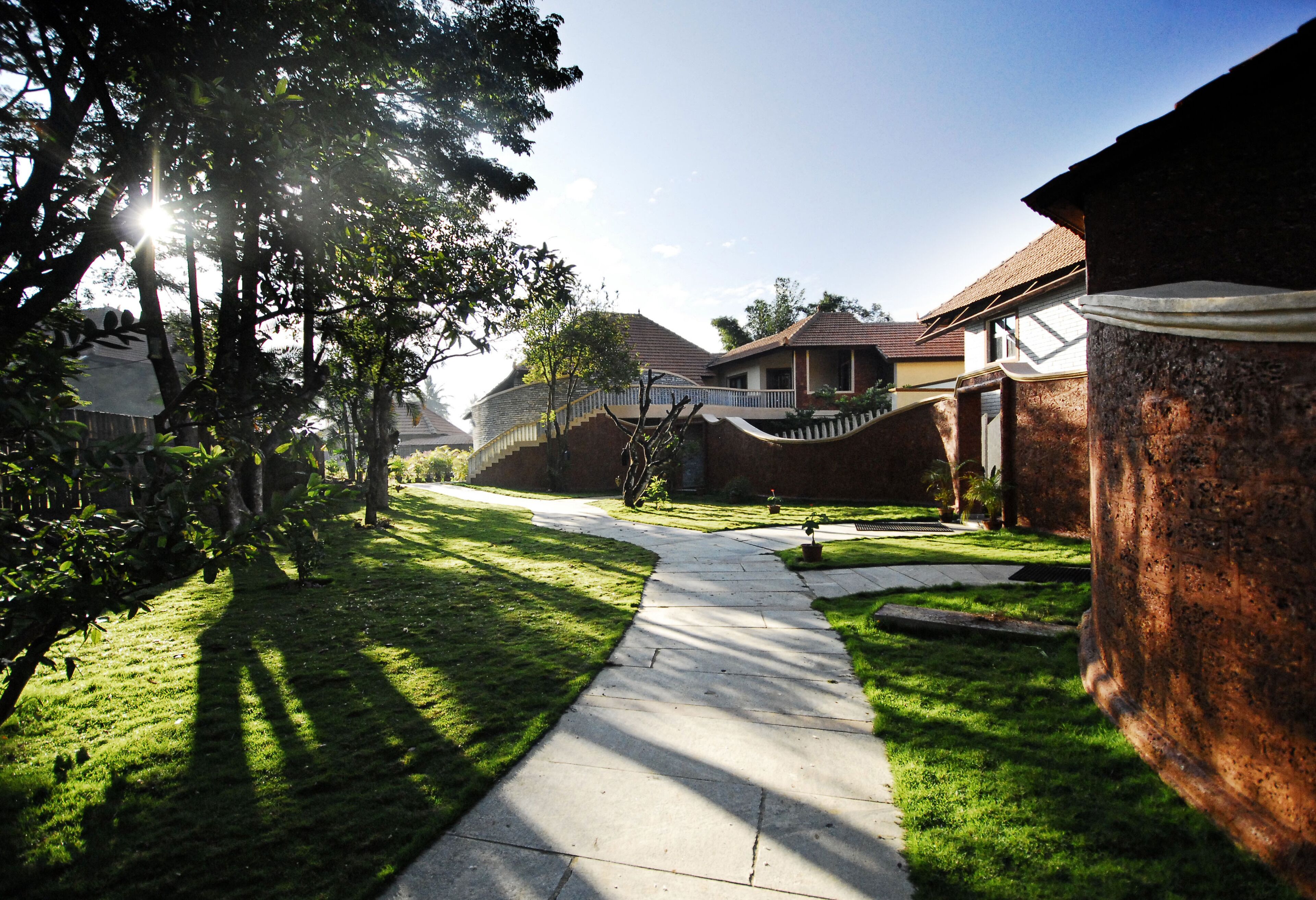 A residential area with a paved pathway, houses, and a large tree casting shadows.