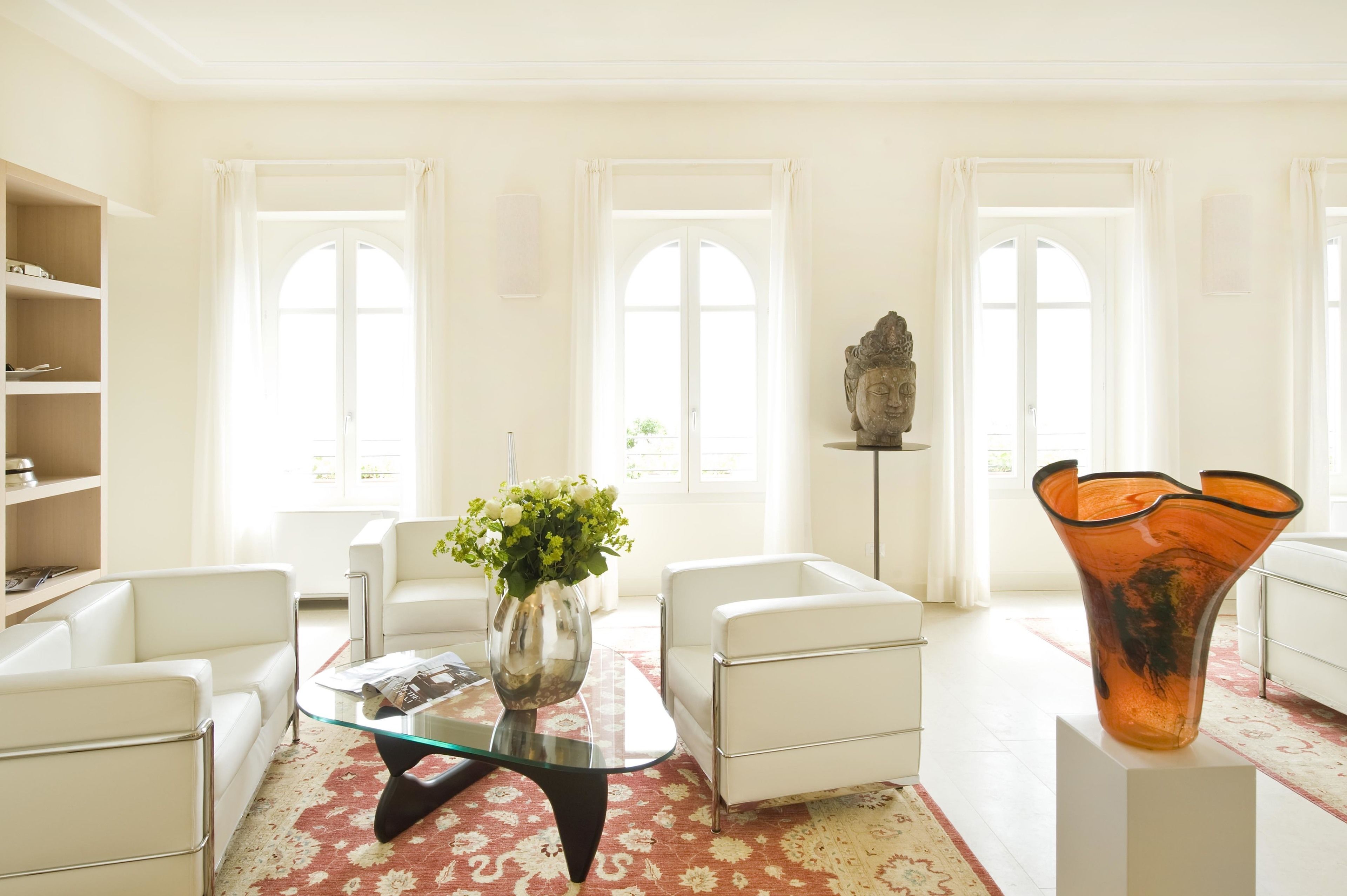 A modern living room with white furniture, a glass coffee table, and a vase with flowers.
