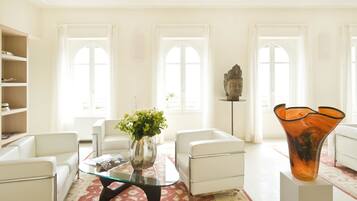 A modern living room with white furniture, a glass coffee table, and a vase with flowers.