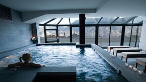 Zona de spa con hidromasaje y asientos, amplias ventanas con vistas a la montaña.