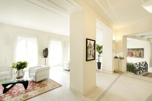 A spacious living room with a white sofa, a glass coffee table, and a red patterned rug. A potted plant and a framed picture are on the wall. - Novessentia (Ghiffa)