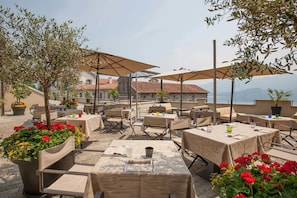 An outdoor café with tables and chairs, umbrellas, and potted plants. - Novessentia (Ghiffa)