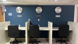 Um espaço de escritório moderno com cubículos, três relógios e placas indicando 'México', 'Nova York' e 'Paris'.