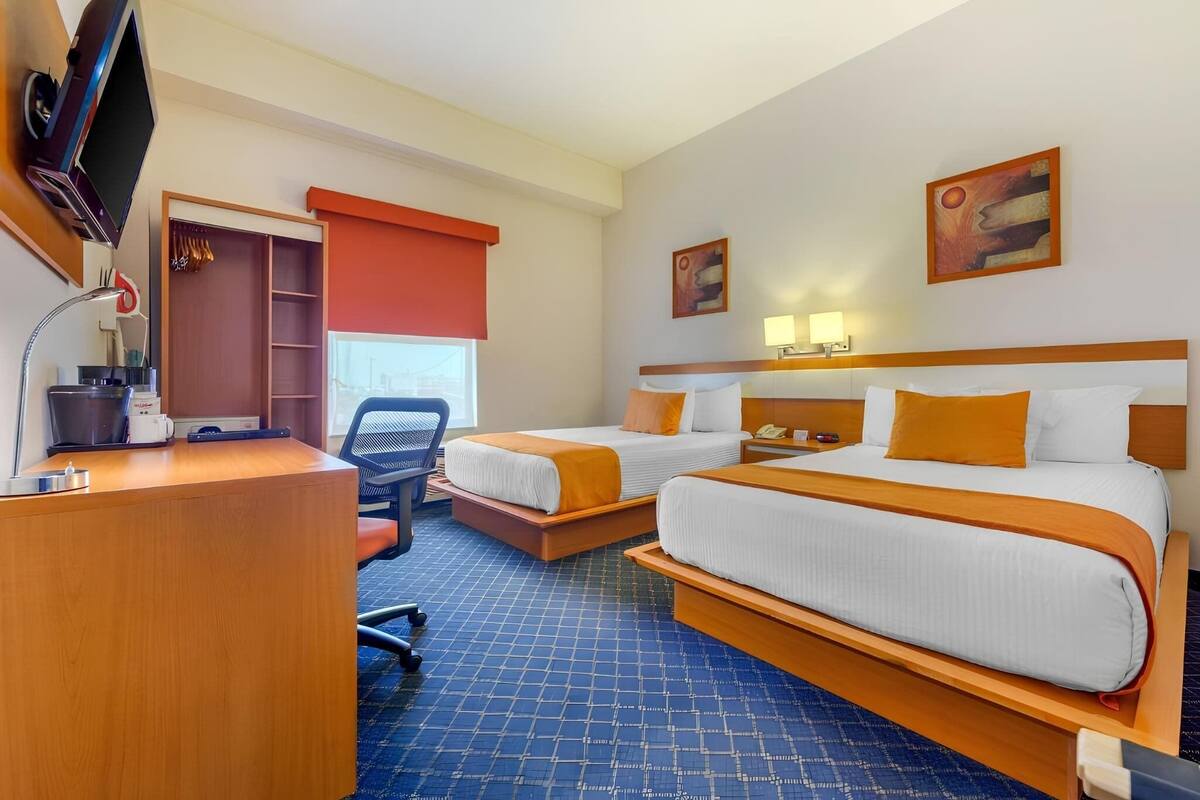 A hotel room with two beds, a desk, a chair, a TV, and a closet.