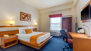 Quarto de hotel com cama, mesa de cabeceira com telefone, escrivaninha com cadeira, televisão e janela com vista.