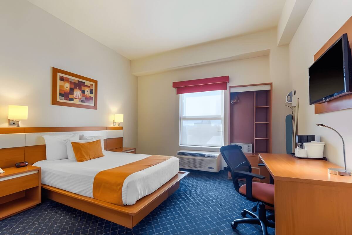 A hotel room with a bed, bedside table with a phone, a desk with a chair, a TV, and a window with a view.