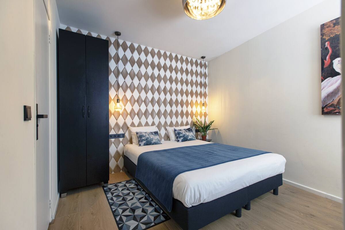 A bedroom with a bed, a wardrobe, a patterned wall, and a painting.