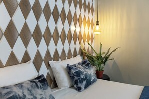 A neatly made bed with white and blue patterned pillows, a potted plant, and a geometric patterned wall. - Quentin Leidse Square Hotel (Amsterdam)