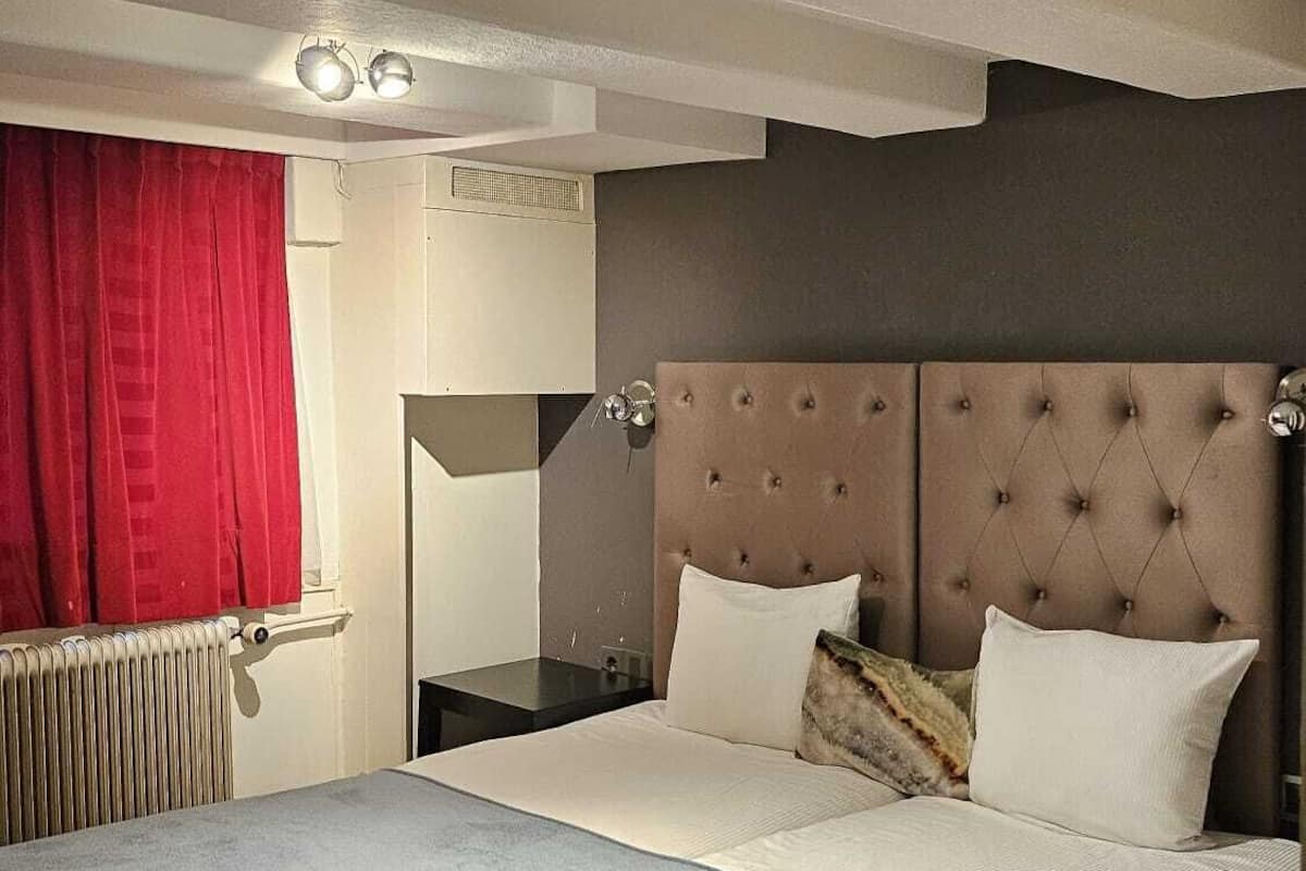 A bedroom with a large bed, a red curtain, a radiator, and a ceiling light.
