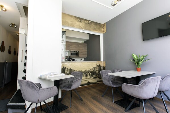 A modern dining area with a white table, four grey chairs, and a potted plant. - Quentin Leidse Square Hotel (Amsterdam)