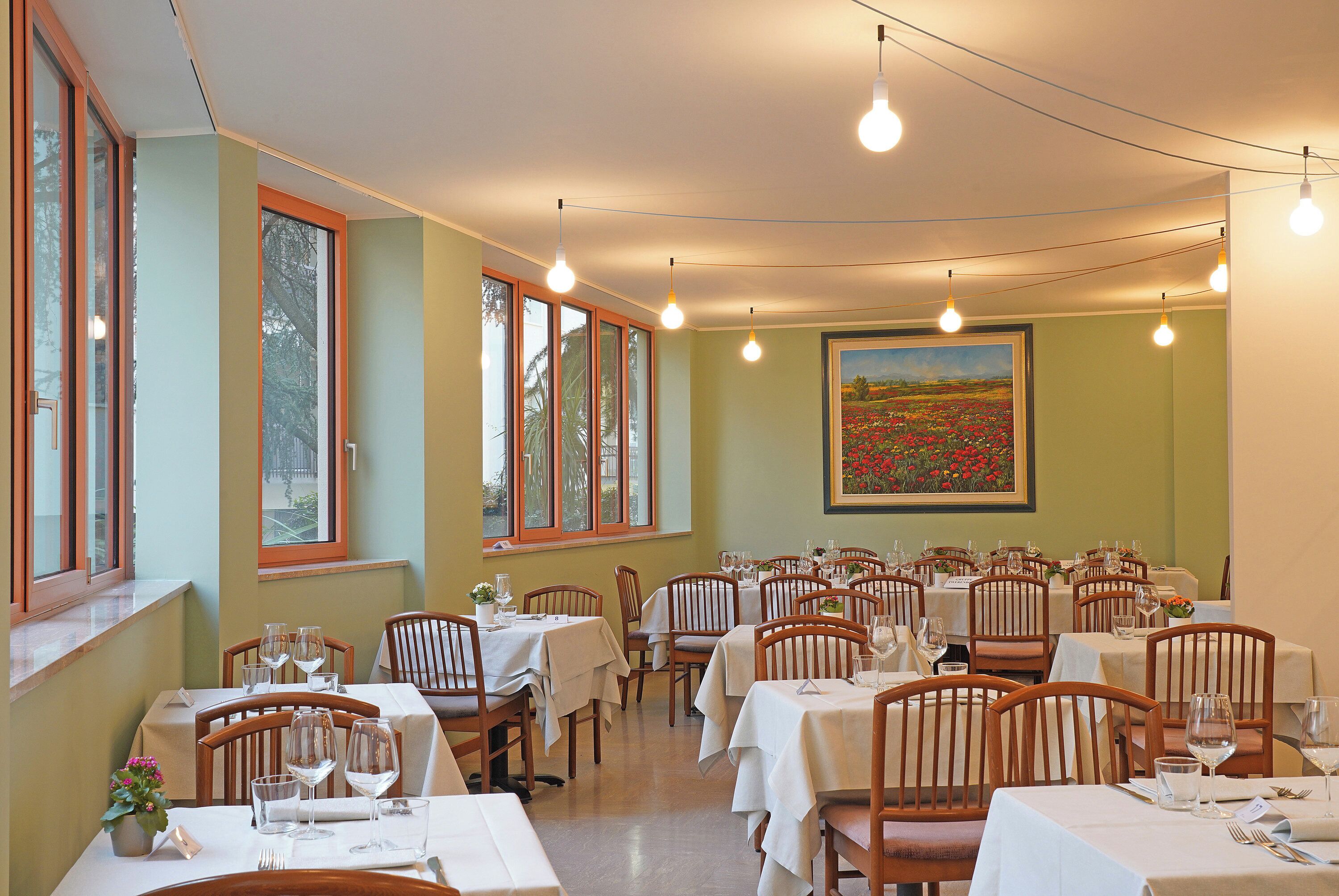 A restaurant with multiple tables and chairs, large windows, and hanging light bulbs.