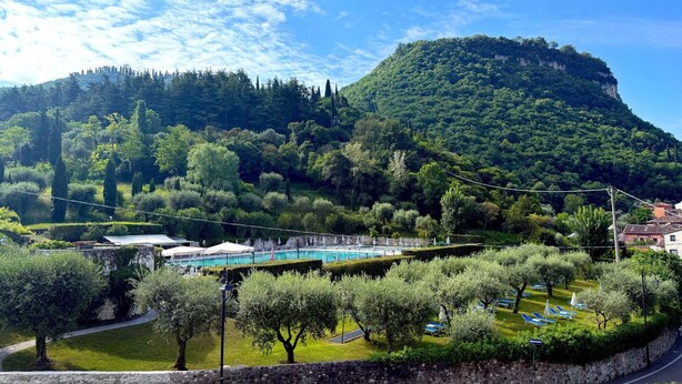 A mountainous landscape with a pool area, trees, and a stone wall. - Bike Hotel La Perla (Garda)
