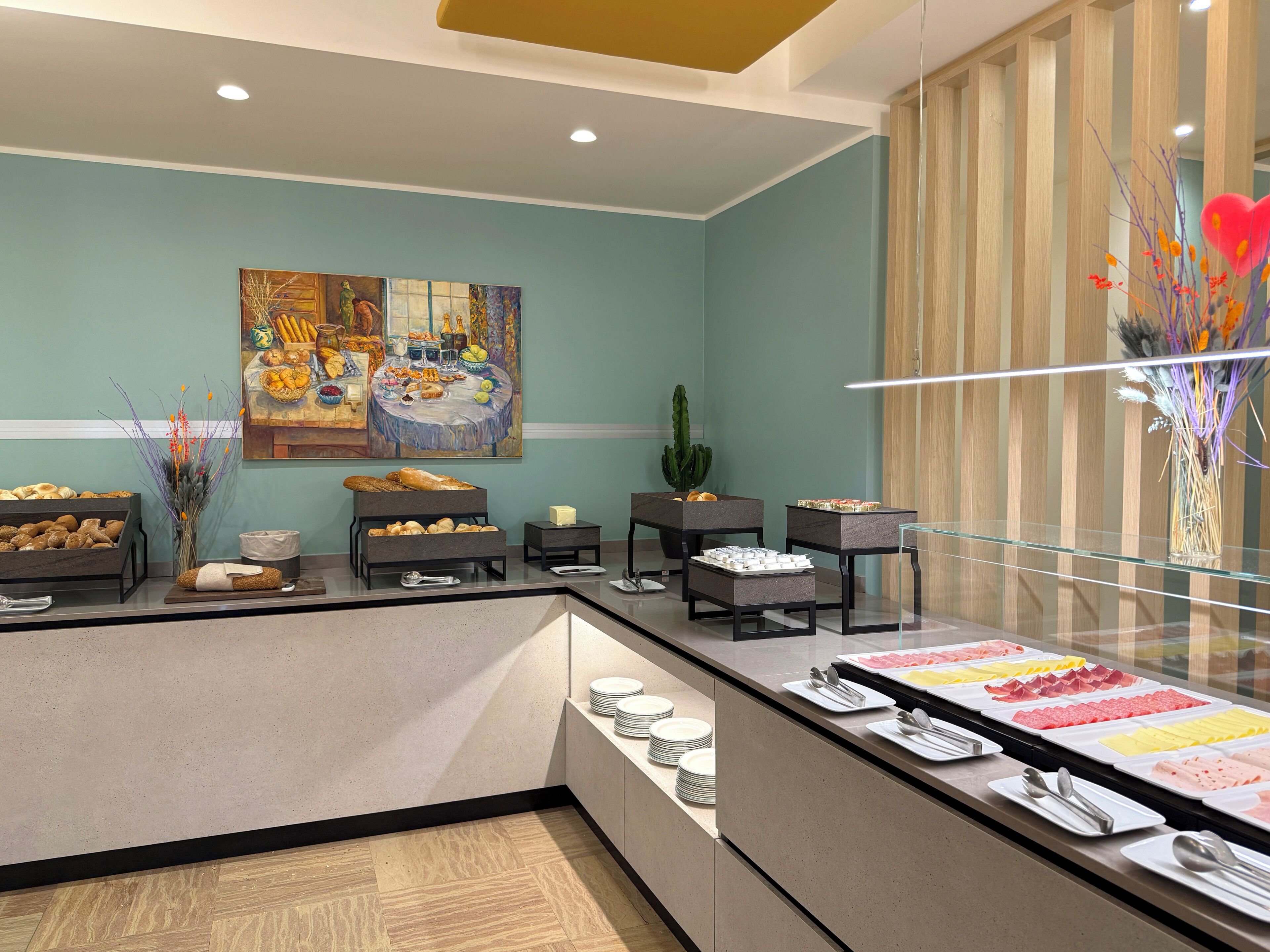 Disposição de buffet com diversos alimentos, uma pintura na parede e uma planta de cacto.