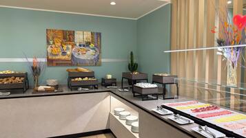 Disposição de buffet com diversos alimentos, uma pintura na parede e uma planta de cacto.