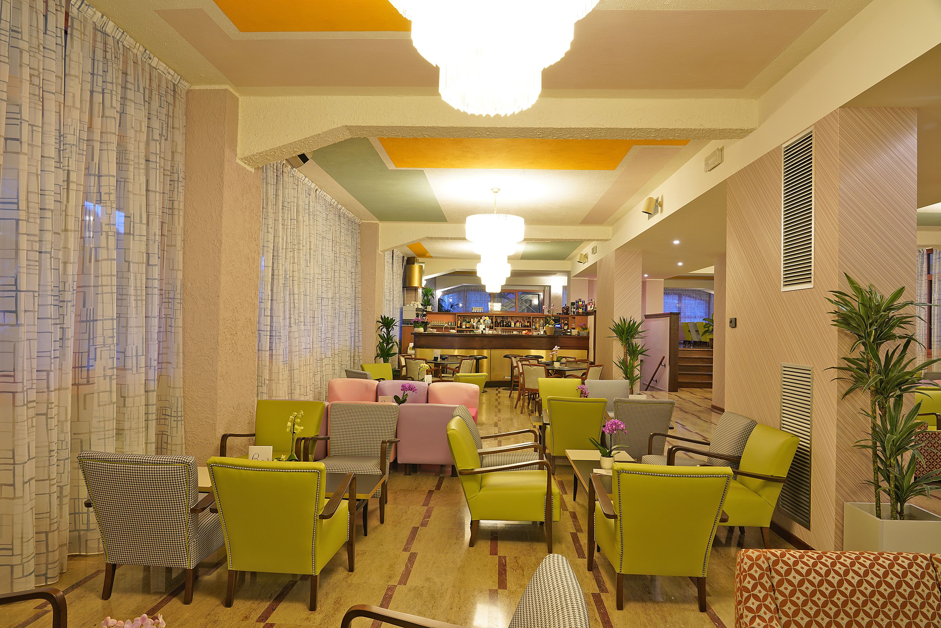 Vestíbulo de hotel con zona de bar, diversas opciones de asientos, incluyendo sillas y sofás, y un techo decorativo.