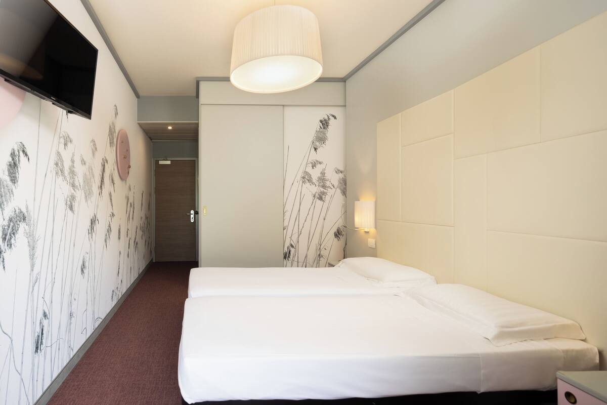Une chambre d’hôtel équipée d’un lit, d’un téléviseur à écran plat fixé au mur et d’une lampe également fixée au mur.