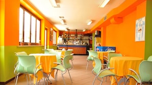 Un restaurante de colores llamativos, con paredes anaranjadas y verdes, manteles amarillos y sillas verdes.