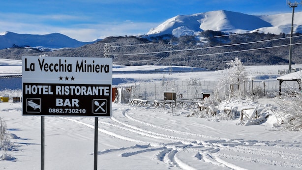 Señal para el Hotel Ristorante Bar La Vecchia Miniera, con un paisaje de montaña nevada.