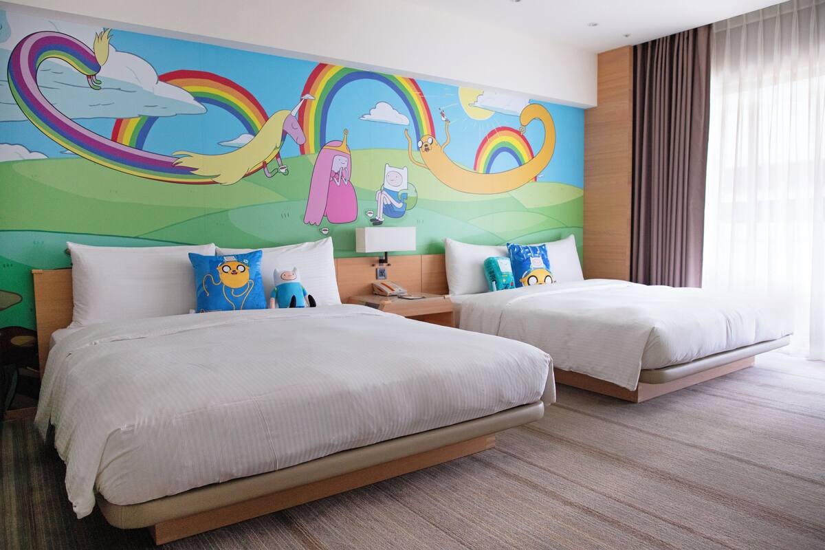 A hotel room with two beds, a mural on the wall, and a window with curtains.