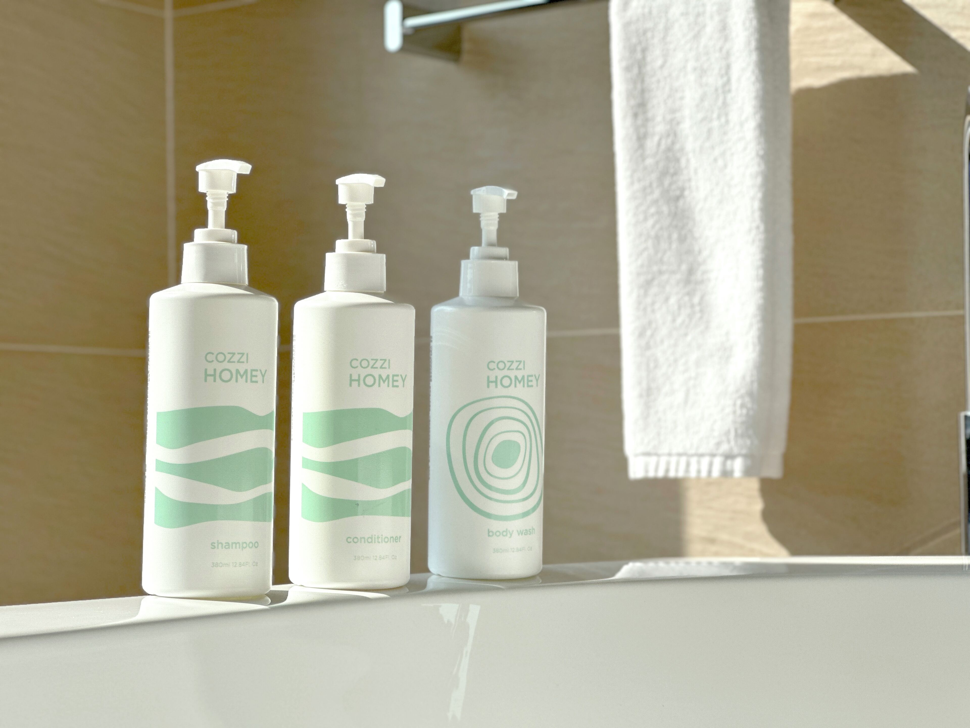 Drie flessen Cozzi Homey shampoo, conditioner en douchegel op een badkamermeubel.