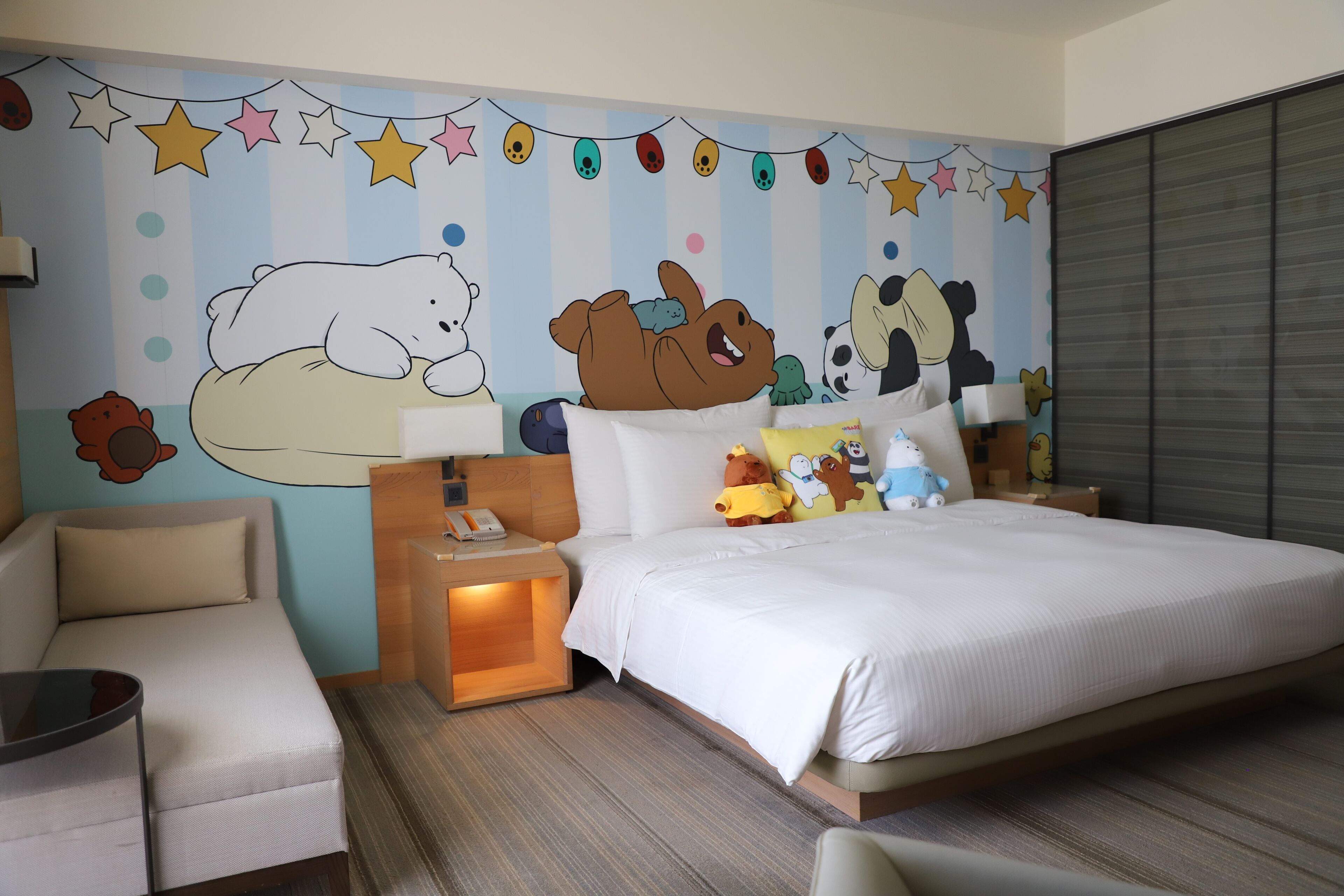 A hotel room with a bed, a sofa, a nightstand, and a wall mural.