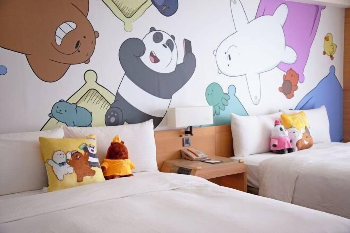 A hotel room with two beds, a nightstand, and a wall with cartoon characters.