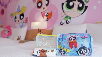 A bed with pillows, a bedside table with a lamp, and a wall with cartoon characters.