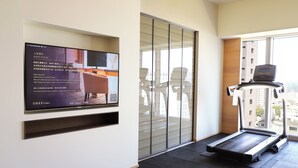 A modern hotel room with a large flat-screen TV mounted on the wall, a treadmill, and a large window offering a city view. - HOTEL COZZI Ximen Tainan (Tainan)