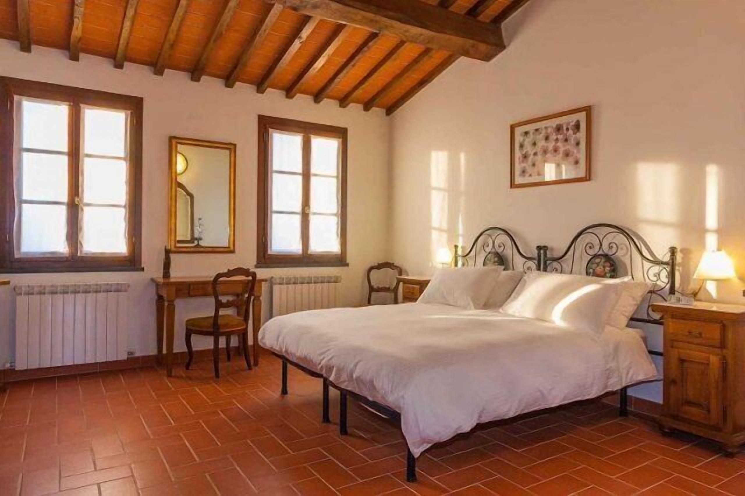 A bedroom with a bed, wooden headboard, two bedside tables, a chair, and a radiator.