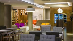 A modern lobby with seating areas, a reception desk, and a beverage refrigerator. - DMax Hotel (Marilia)